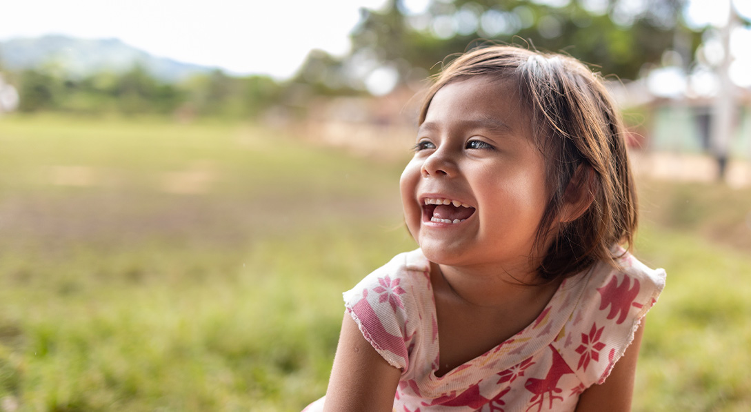 Young girl sitting in a field laughs while looking to the right.