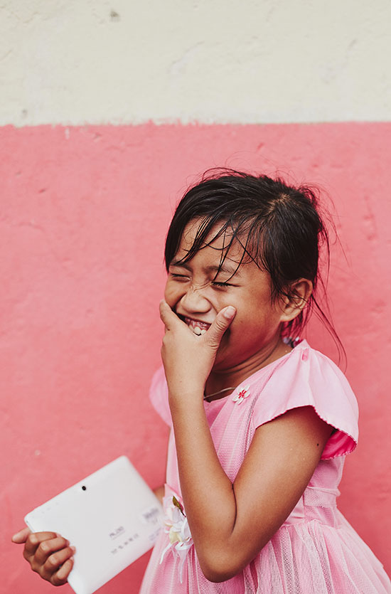 A girl in a pink dress covers her mouth with her hand as she laughs